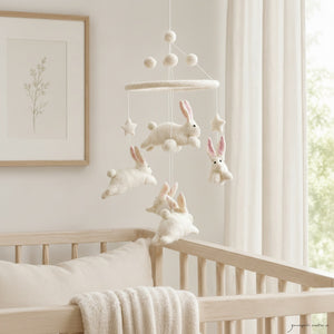This felt bunny mobile hanging above a light wood crib in a calm, bright nursery with soft window light