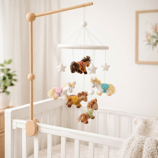 Felt pony mobile viewed from a low angle against a softly blurred cream wall in warm light.