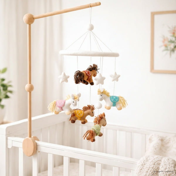 Felt pony mobile hanging above a light wood crib in a calm, bright nursery with soft window light.