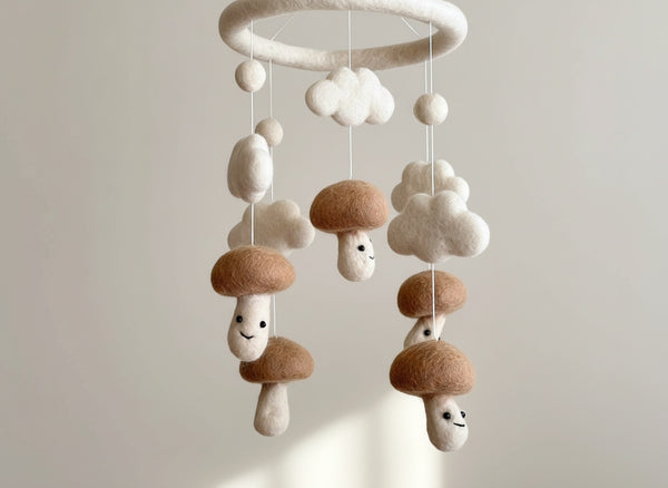 Low angle close up of the felt mushroom baby mobile against a softly blurred cream wall in warm light