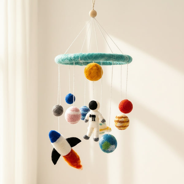 Close up view of the felt solar system baby mobile from a low angle against a soft cream wall.