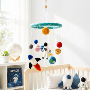 Felt solar system baby mobile hanging above a light wood crib in a bright, calm nursery.