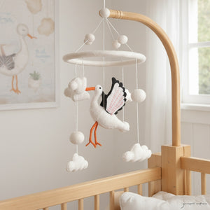 Felt stork mobile hanging above a light wood crib in a calm, bright nursery with soft window light.