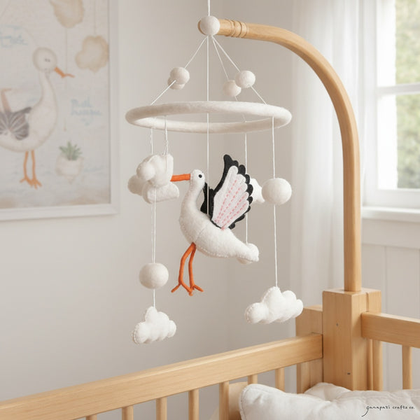 Felt stork mobile hanging above a light wood crib in a calm, bright nursery with soft window light.