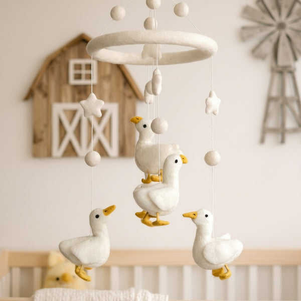 Close-up of the felt duck baby mobile from a low angle against a softly blurred cream wall.