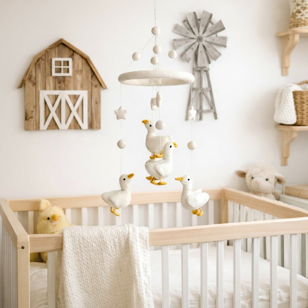 Felt baby mobile with white duck hanging above a light wood crib in a calm, bright nursery.