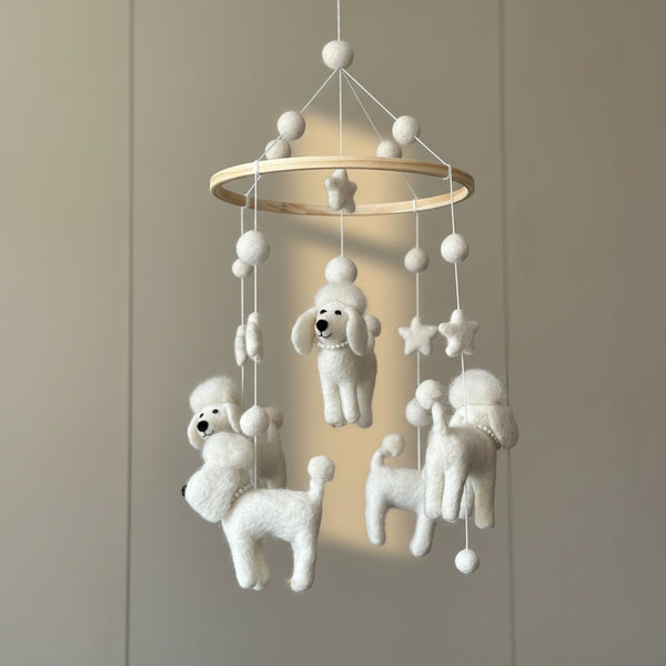 Close-up view of the white poodle felt baby mobile against a softly blurred cream wall.