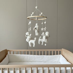 White poodle felt baby mobile hanging above a light wood crib in a bright, calm nursery.