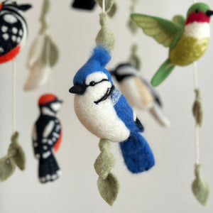 Low angle close-up of felt birds and leaf strands against a soft cream wall