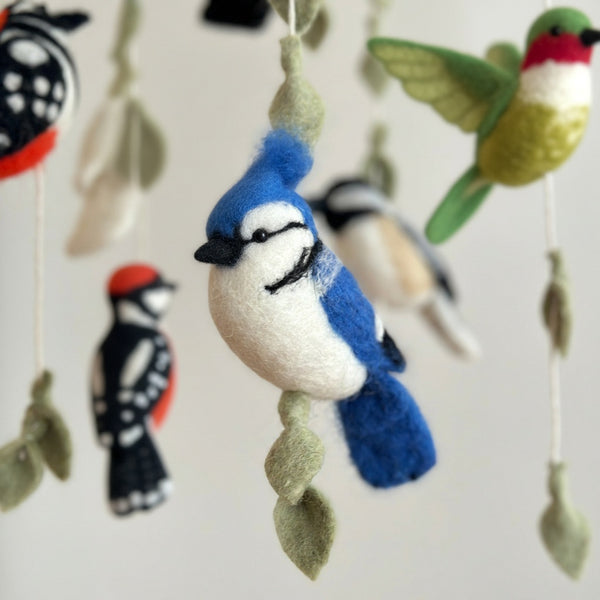 Low angle close-up of felt birds and leaf strands against a soft cream wall