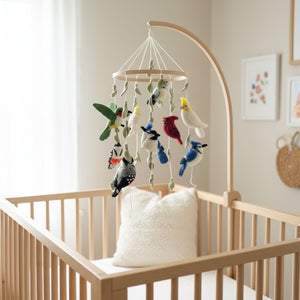 Felt bird mobile with cardinal and blue jay hanging above a crib in a calm nursery