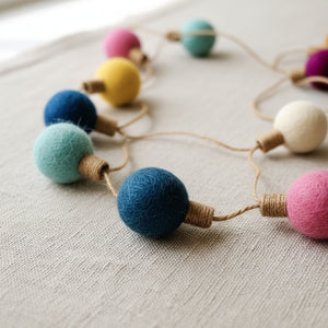 Close up of felt color ball garland on linen, showing wool felt texture and jute string