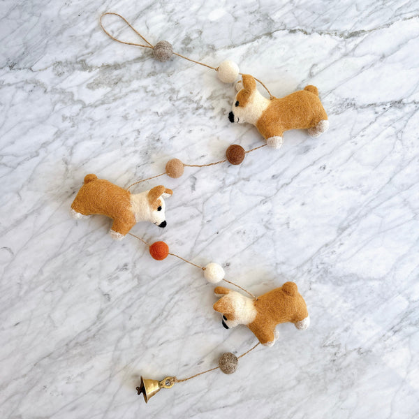 Felt corgi garland laid flat on a marble surface showing the felt texture and small bell