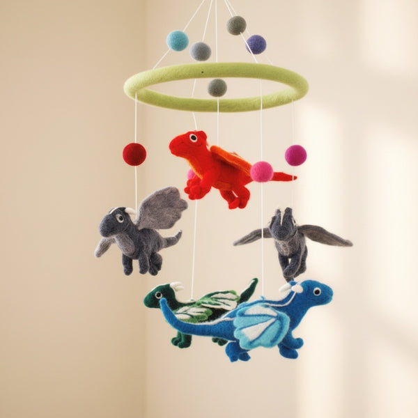 Close up of felt dragon baby mobile from a low angle against a soft cream wall