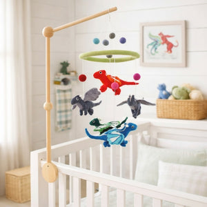 Felt dragon baby mobile hanging above a light wood crib in a calm, bright nursery