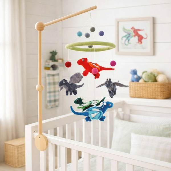 Felt dragon baby mobile hanging above a light wood crib in a calm, bright nursery