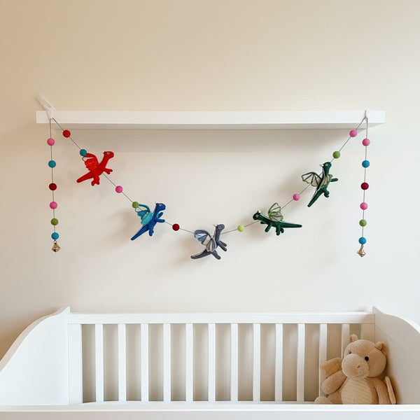 Felt dragon garland draped along a nursery shelf above a crib in soft daylight