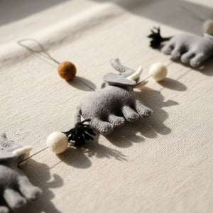 Close-up of the felt elephant garland's wool texture and pom poms on a light linen surface