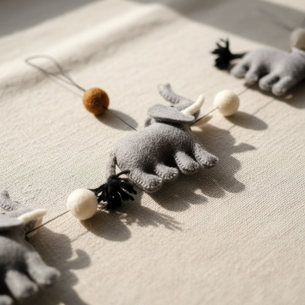 Close-up of the felt elephant garland's wool texture and pom poms on a light linen surface