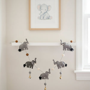 This felt elephant garland draped along a shelf in a calm, sunlit nursery with neutral walls
