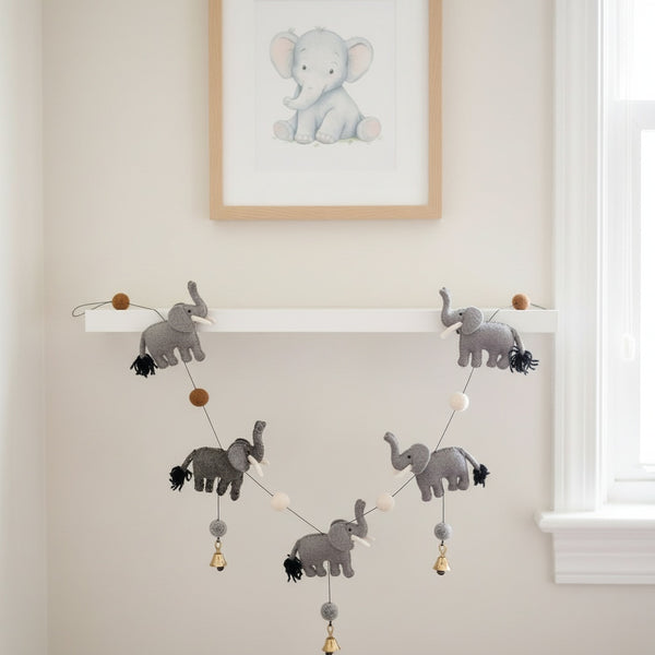 This felt elephant garland draped along a shelf in a calm, sunlit nursery with neutral walls