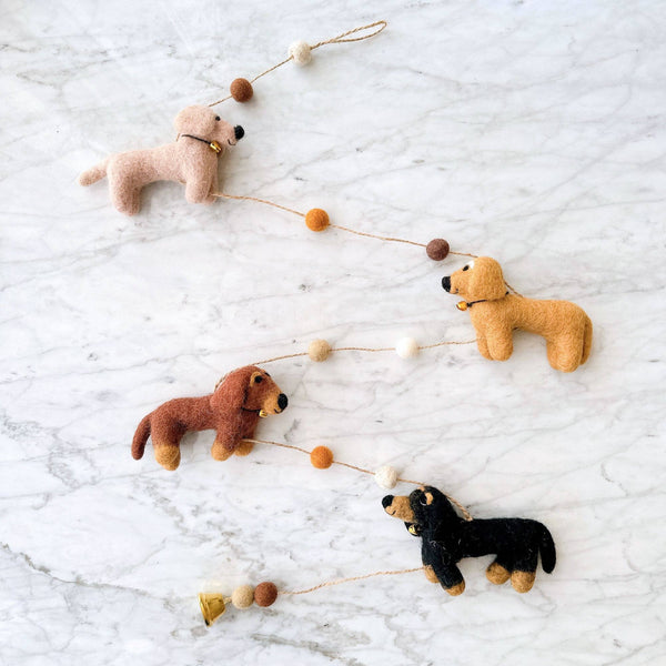 Four felt dachshund dogs and pom bead details from the garland arranged flat on a marble surface.