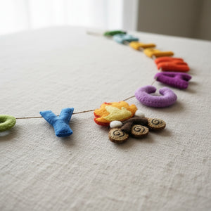 Close-up of the Happy Camper felt garland resting on linen, showing the texture of the felt letters