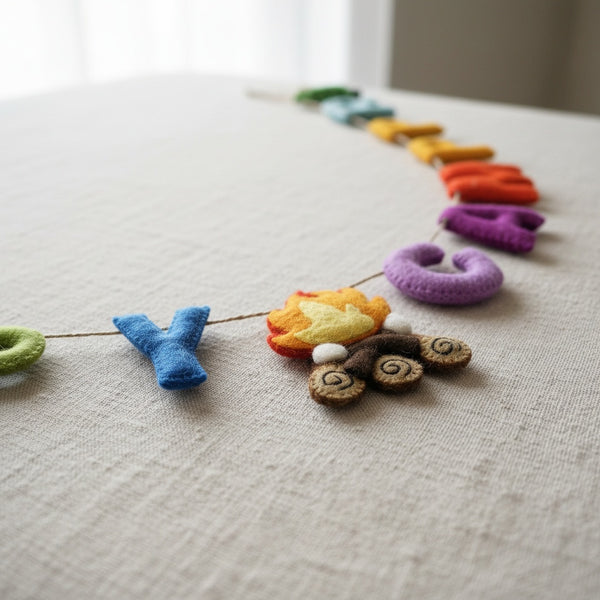Close-up of the Happy Camper felt garland resting on linen, showing the texture of the felt letters