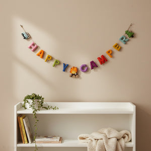 Happy Camper felt garland draped above a crib in a calm nursery with soft daylight and neutral walls
