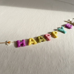 Close-up of felt Happy Easter garland's stitched letters lying on a linen surface