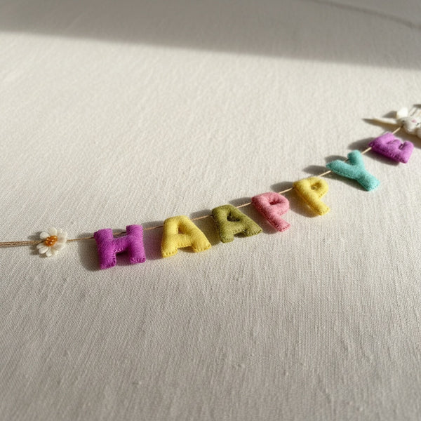 Close-up of felt Happy Easter garland's stitched letters lying on a linen surface