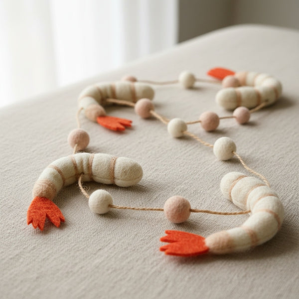 Close-up of the felt shrimp garland on a linen surface, showing the soft felt texture and stitching