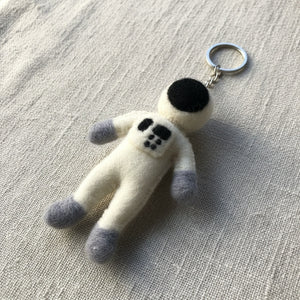 Felt astronaut keychain resting on a linen surface, close-up showing the wool felt texture.