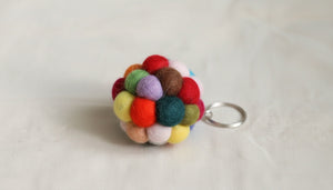 Close up of a felt pompom ball keychain on light linen, showing the handmade wool texture