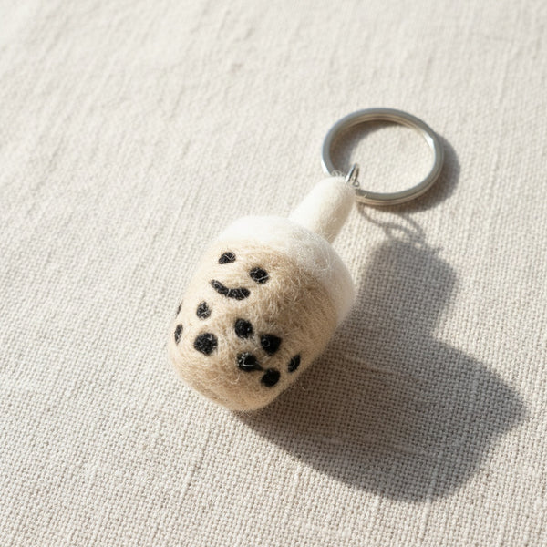 Close-up of a felt boba tea keychain on light linen, showing hand-stitched felt texture