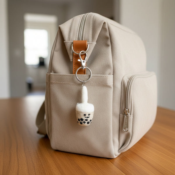 Felt boba tea keychain clipped to a canvas diaper bag on a wooden table in daylight