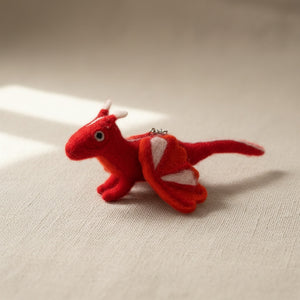 Felt dragon keychain resting on light linen, close up on the wool felt texture