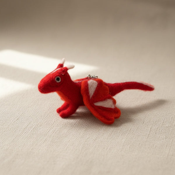 Felt dragon keychain resting on light linen, close up on the wool felt texture
