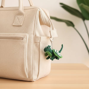Felt dragon keychain clipped to a canvas diaper bag on a wooden table in daylight