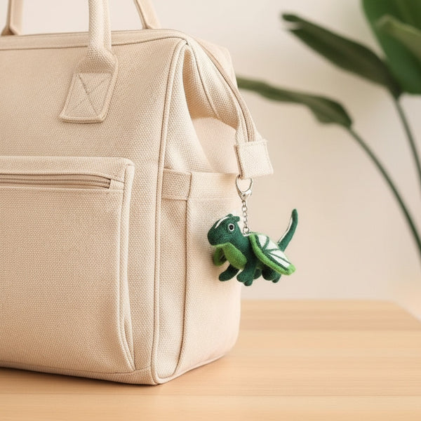 Felt dragon keychain clipped to a canvas diaper bag on a wooden table in daylight