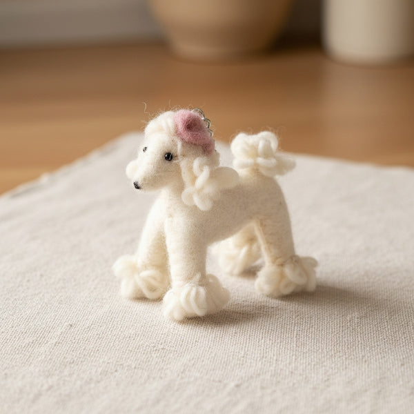 Felt poodle keychain resting on light linen fabric, showing its soft wool texture up close.