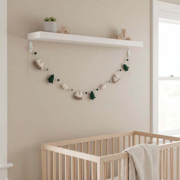 Felt mountain and cloud garland draped along a white nursery shelf in soft daytime light