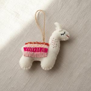 Close-up of the felt llama ornament's wool texture and stitched saddle on linen fabric