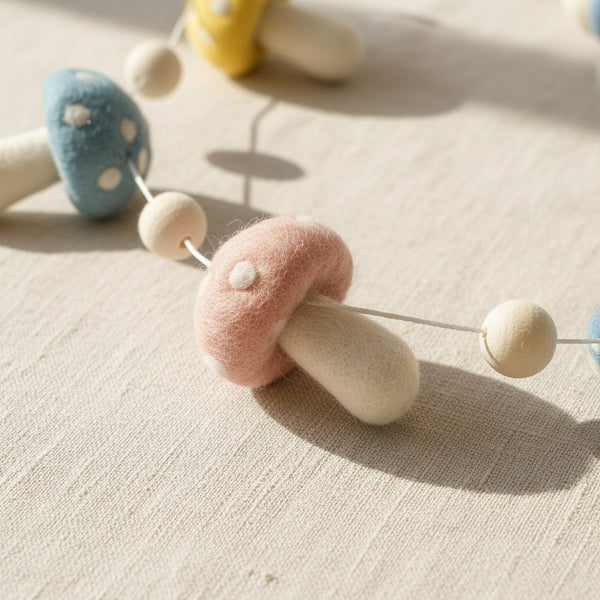 Close up of felt pastel mushroom garland resting on light linen, showing soft wool felt texture.