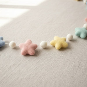 Close-up of a felt pastel star garland resting on light linen, showing soft wool felt texture