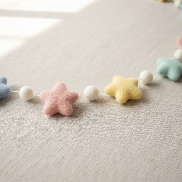 Close-up of a felt pastel star garland resting on light linen, showing soft wool felt texture
