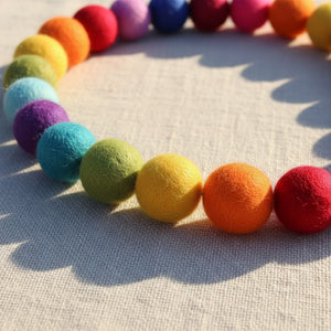 Close up of felt rainbow pompom garland on linen, showing needle felted wool texture.