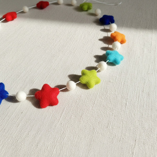 Close-up of the felt star garland on linen fabric, showing the texture of the rainbow felt stars