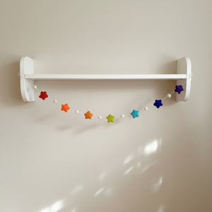 Felt star garland draped along a white nursery shelf, adding soft rainbow color to the room