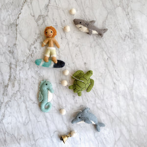 Closeup of felt surfer, shark, turtle, seahorse, and dolphin figures from the garland laid on a marble surface